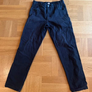Svarta byxor från Dickies (strl W30/L32) - Säljer ett par svarta cargopants från Dickies med raka ben och klassiska cargofickor baktill. Byxorna har normal passform, bälteshällor och är tillverkade i slitstark bomull. Perfekta för en streetwear-look eller chill vardagsstil. Storlek W30/L32.