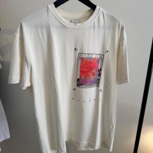 Vit t-shirt från Zara med grafiskt tryck - Vit t-shirt i bomull med coolt grafiskt tryck framtill i rött, lila och svart samt tryck på ryggen med text och palm-motiv. Klassisk passform och rund halsringning. 