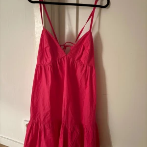 Rosa sommarklänning - Snygg rosa klänning med smala axelband och v-ringning. Klänningen har volang nertill och knytning i ryggen för extra detalj. Perfekt för varma dagar och ger en avslappnad men trendig look. Säljer då den är lite för stor för mig. 