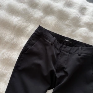 Svarta bootcut-byxor från Bikbok - Snygga svarta byxor från Bikbok med bootcut-modell och klassisk passform. Byxorna har hällor för bälte och sidfickor, perfekta för en stilren look. Materialet är mjukt och följsamt, vilket gör dem bekväma att bära hela dagen.