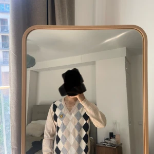 Beige argyle mönstrad tröja från Lyle & Scott - Säljer en stilren beige tröja från Lyle & Scott med klassiskt argyle mönster i grått och svart. Tröjan har en v-ringad hals och ett broderat emblem på bröstet. Perfekt för en elegant och avslappnad look.