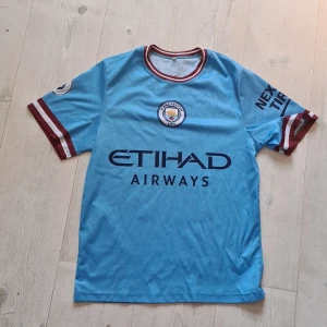 Manchester City tröja - Snygg Manchester City fotbollströja med Haaland och nummer 9 på ryggen. Tröjan är ljusblå med vinröda och vita detaljer på ärmslut och krage. Officiell klubbmärke på bröstet och Etihad Airways-tryck framtill. Tillverkad i lätt och ventilerande material. Tröjan är strl 152, jag har knappt använt då den är för liten och det faktum att jag hejar på Barcelona. Fick i present.