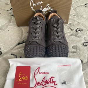 Christian Louboutin grå mocka sneakers - Säljer dessa Christian Louboutin sneakers i mörkgrå mocka med ikoniska nitar framtill. Använda endast 2 gånger, vilket syns tydligt – skicket är nära nyskick! Supersnygga, trendiga och lyxiga sneakers. Svarar gärna på frågor 🙂