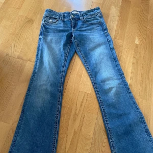 Blå bootcut jeans från Gina Tricot - Snygga blå jeans från Gina Tricot i storlek 158. Modellen har bootcut-ben, klassiska fickor med lock och knapp bak samt coola slitningar framtill. Jeansen är i mjukt denimtyg och har normal passform. Perfekta till sneakers eller boots.