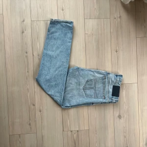 Ljusblå jeans från Tiger of Sweden, Nico - Säljer ett par ljusblå jeans från Tiger of Sweden med klassisk femficksdesign och raka ben. Jeansen har snygga kontrastsömmar och en stilren patch bak i midjan. Perfekta för dig som gillar en clean och tidlös look.