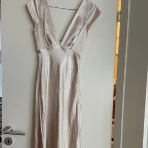 Champagnefärgad långklänning med v-ringning - Champagnefärgad balklänning av satin. Djup v-ringning både fram och bak samt en öppen detalj i ryggen. Klänningen har figurnära passform. Använd en gång. Köpt från Billy J, nypris 920. Vid intresse eller frågor kontakta gärna mig☺️