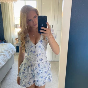 Blommig kortklänning från Zara - Supersöt kortklänning från Zara med volanger, v-ringning och puffärmar. Vit botten med blått blommönster, perfekt för sommarens alla tillfällen. Lätt och luftig i bomull, ger en romantisk och fräsch vibe.