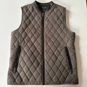 Quiltad grå grön från Zara Man - Snygg quiltad väst från Zara Man i grönt med svarta detaljer. Västen har dragkedja framtill och två fickor med dragkedjor. Perfekt lager-på-lager-plagg med stilren look och lätt vaddering.