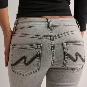 Low Waist Bootcut Stitch Jeans - Snygga grå jeans med bootcut passform och coola broderade detaljer på bakfickorna. Jeansen har klassisk femficksdesign, bälteshällor och är tillverkade i mjukt denimtyg. Perfekta för dig som gillar en retrovibe och vill sticka ut lite extra.