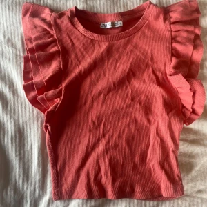 Rosa volangtopp från Zara - Supersöt rosa topp från Zara med volangdetaljer på axlarna. Ribbad struktur och ärmlös design ger en trendig och lekfull look. Perfekt att styla med jeans eller kjol för en färgstark outfit. 💕