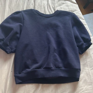 Mörkblå kortärmad tröja Gina Tricot - En basic mörkblå tröja från Gina Tricot med korta ärmar och ribbade muddar vid hals, ärmslut och nederkant. Perfekt för dig som gillar en enkel och stilren look. Skön och mjuk, passar till det mesta.