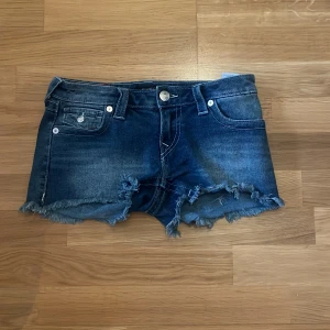 True Religion jeansshorts Joey Cut-Off - Snygga blå jeansshorts från True Religion, modell Joey Cut-Off. Lågmidjade med fransiga kanter och klassiska fickor både fram och bak. Endast använda 3 gånger. Pris kan diskuteras