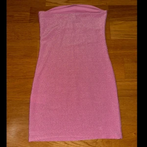 Rosa glittrig axelbandslös klänning - Snygg rosa axelbandslös klänning med glittrigt material. Perfekt för en kväll ute eller vid annat speciellt tillfälle. Den korta längden ger en trendig look. (Återpublicerad)