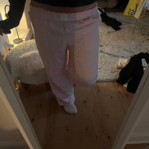 Rosa-vit randiga mysbyxor  - Säljer ett par mysiga rosa och vita randiga byxor med resår i midjan. De har en loose passform och raka ben, perfekta för en mysig outfit!! Har tagit bort lappen så vet tyvärr ej var dom är köpta. Nypriset är 200🥰