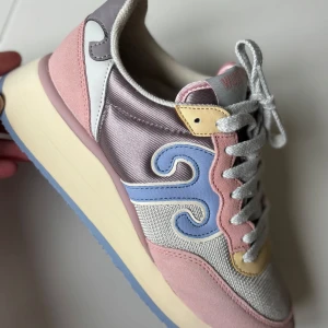 Pastellfärgade sneakers från Wushu - Snygga sneakers från Wushu i pastellfärger med rosa, lila, blå och gula detaljer. Ovandel i textil och mocka, med vågig blå detalj på sidan och grå snörning. Tjock, beige sula med blå undersida. Perfekta för dig som gillar färg och unik stil. Extra snören tillkommer, bild. (Obs:prislapp-danska kronor=1942;- ) Var någon besserwisser som inte förstod det på blocket och var tyvungen att kommentera priset jag lagt (utan intresse av varan😴) 