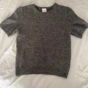Grå stickad kortärmad tröja H&M XS - Mysig grå stickad tröja från H&M i storlek XS. Tröjan har korta ärmar, rund halsringning och ribbade muddar vid ärmslut och nederkant. Perfekt för lager-på-lager och enkel att matcha med jeans eller kjol.