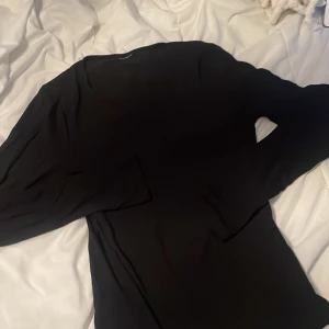 Svart långärmad blus - En stilren svart blus med långa ärmar. Enkel och klassisk design som passar perfekt när du vill ha en clean look. Mjuk och följsam känsla i materialet, vilket gör den bekväm att bära hela dagen.