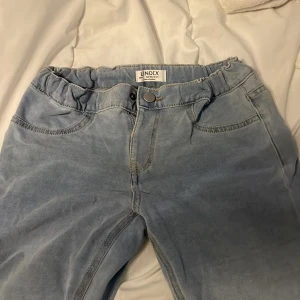 Ljusblå bootcut jeans från Lindex - Säljer ett par ljusblå jeans från Lindex med bootcut-ben och resår i midjan. Jeansen har klassiska fickor fram och bak, knapp och dragkedja. Slim passform upptill och tillverkade i mjuk bomull med jeanskänsla.
