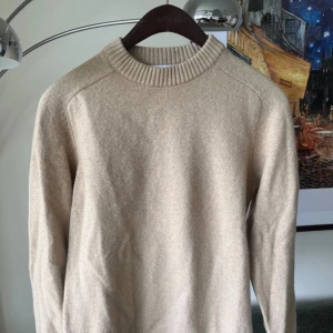 Beige stickad tröja från Selected Homme - Beige stickad tröja från Selected Homme med rund halsringning och bred ribbad kant. Tröjan är långärmad och har en clean, klassisk look som funkar till allt. Materialet är en mix av ull och nylon vilket gör den både mjuk och lätt att bära.