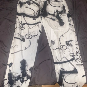Graffiti-inspirerade jeans från Sweet SKTBS - Unika vita jeans från Sweet SKTBS med svart graffiti-liknande print över hela byxan. Raka ben och klassisk femficksmodell. Jeansen är tillverkade i Denim och har en streetig vibe med konstnärliga detaljer. Perfekta för dig som vill sticka ut.