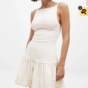 Vit kort klänning med volangkjol - Supersöt vit kortklänning med figurnära överdel och volangkantad kjol. Klänningen har smala axelband och är ärmlös, perfekt för varma dagar. Materialet ser ut att vara mjukt och lätt, vilket ger en skön känsla och snygg passform.