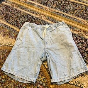 Ljusblå jeansshorts från H&M - Säljer ett par ljusblå jeansshorts från H&M i regular fit. De har elastisk midja med vit snörning och klassisk femficksdesign. Perfekta för chill dagar och enkel att matcha med t-shirt eller hoodie.