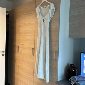 Vit långklänning med volangärm - Luftig vit långklänning från Lager 157 med snygg struktur, volangärmar och knytning framtill. Klänningen har en lätt v-ringning och slits framtill. Aldrig använd!