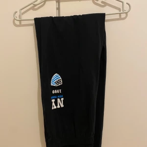 Svarta mjukisbyxor med NY-tryck - Mörkblåa mjukisbyxor med elastisk midja och tryck på ena benet med texten 'NY New York 1999' och en blåvit sköld. Sköna och enkla byxor i bomull.