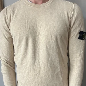 Beige långärmad tröja från Stone Island - Snygg beige långärmad tröja från Stone Island med klassisk patch på vänster ärm. Tröjan har rund halsringning och är tillverkad i mjuk bomull. Säljer då jag inte har användning längre. 9/10, bra skick. storlek M