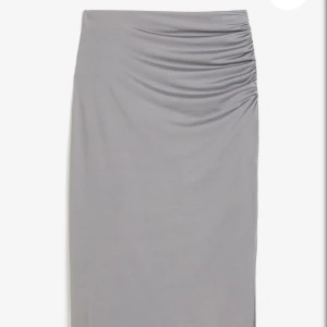 Grå långkjol  - Snygg grå långkjol med slits i mjukt och stretchigt material med rynkade detaljer vid midjan. Kjolen har en clean look och passar perfekt till sneakers eller boots. Enkel att styla med både crop top och oversized tröja.