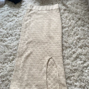 Beige stickad långkjol från H&M - Säljer en beige stickad långkjol från H&M med snyggt hålmönster och strech material i midjan. Kjolen har en slits framtill som ger en extra cool touch. Perfekt för dig som gillar en chill och trendig stil. Perfect för stranden💕
