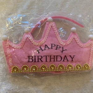 LED Diadem Happy Birthday krona rosa/blå - Fira med ett diadem i form av en krona med texten 'Happy Birthday'. Finns i rosa och blått, dekorerad med paljetter, pärlor och guldfärgade detaljer. Tillverkad i filt och plast, perfekt för födelsedagsfirande och festliga tillfällen. LED lampor med 7 färger, 59kr/st 