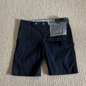 Mörkblå shorts Polo Ralph Lauren - Snygga mörkblå shorts från Polo Ralph Lauren i slim fit-modell med stretch. Klassisk design med två fickor fram, två bakfickor med knappar och bälteshällor. Perfekta för sommaren och riktigt clean look. De köptes på Ralph lauren store i Berlin, jag har kvar påsen. Priset är inte hugget i sten och kan sänkas drastiskt vid en snabb affär