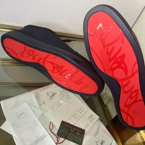 Mörkblå sneakers från Christian Louboutin - Snygga mörkblå sneakers från Christian Louboutin i mocka med ikoniska röda sulor och broderad logga baktill. Skorna har rund tå, snörning och beige innersula. Perfekta för dig som vill sticka ut med exklusiv stil och detaljer. Går såklart ner i pris vid snabb affär, A-K