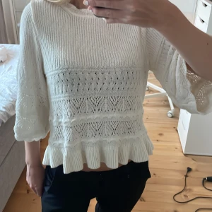 Vit stickad tröja med volang - Superfin vit stickad tröja med breda trekvartsärmar och volangkant nertill. Tröjan har ett detaljerat hålmönster. 