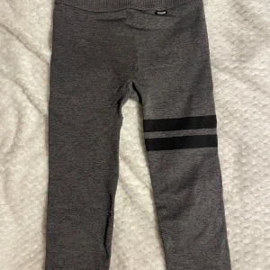 Grå leggings med svarta ränder - Mörkgrå leggings med två svarta ränder på ena benet. Hög midja med ribbad linning för extra komfort. Perfekta för träning eller chill, i mjukt och stretchigt material som sitter tajt och följsamt.