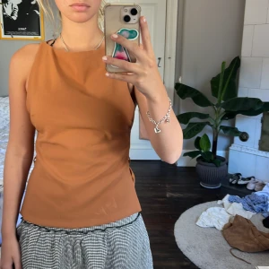 Brun ärmlös topp från Zara - Säljer en snygg brun ärmlös topp från Zara med hög hals och slitsar i sidorna. Toppen har en stilren, rak passform och stängs med dragkedja i ryggen. Perfekt att styla med kjol eller jeans 