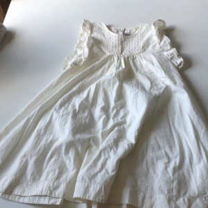 Vit volangklänning Petit Bateau 128cm - Supersöt vit klänning från Petit Bateau i bomull med volangdetaljer på ärmarna och fina veck framtill. Klänningen har knappar i ryggen och en luftig, svängd passform. Perfekt för sommarens alla tillfällen!