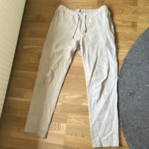 Linnebyxor Beige - Snygga beiga linnebyxor från Dressmann i storlek M. Byxorna har elastisk midja med snörning och raka ben. Tillverkade i en skön linnemix som passar perfekt för varmare dagar. Två bakfickor med knapp och avslappnad passform.