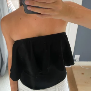 Svart bandeau tubtopp med volang - Säljer en svart bandeau tubtopp med bred volang som kan bäras både axelbandslös och offshoulder. 