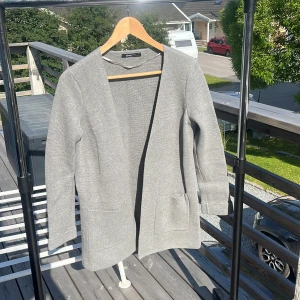 Grå kofta från Gina Tricot i bomull - Snygg grå kofta från Gina Tricot i 100% bomull. Den har öppen front, två stora fickor framtill och långärmad design. Perfekt för lager-på-lager och enkel att matcha med allt. Stilren och enkel modell som funkar året runt.