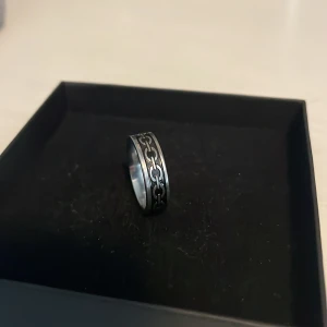 Silverfärgad ring med kedjemönster - Cool ring i silverfärg.Ringen har ett grymt kedjemönster runt hela bandet som ger en edgy vibe. Tillverkad i metall med en bred, rundad form. Perfekt accessoar för dig som vill sticka ut lite extra.