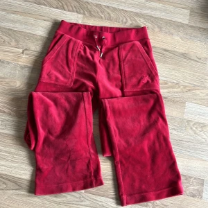Röda mjukisbyxor+hoodie Juicy Couture XS - Röda mjukisbyxor + hoodie från Juicy Couture i mjuk velour med bred resår och snörning i midjan. Byxorna har raka ben, stora fickor fram och bak med knappdetaljer. Perfekta för en chill och trendig look.