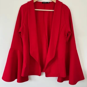 Röd Boohoo kavaj, helt NY - Röd kavaj / jacka / kofta från Boohoo med utsvängda ärmar. Kavajen har en öppen design utan knäppning. Otroligt fin både till vardagsjeans eller när man vill ha det lite mer uppklätt till klänning eller kostymbyxor. Mjuk och skön. Aldrig använd. Storlek L/40.   Hämtas i Stockholm eller skickas mot porto, välj du!