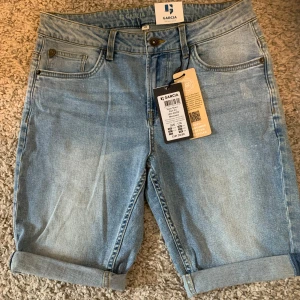 Ljusblå jeansshorts från Garcia - Snygga ljusblå jeansshorts från Garcia med klassisk femficksdesign och uppvikta benslut. Shortsen har bälteshällor och knappgylf, perfekta för en avslappnad stil under varma dagar.