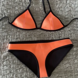 Orange och svart bikini från Triangl - Snygg bikini från Triangl i orange och svart med klassisk triangel-bh och matchande trosor. Bikinin har svarta kanter och är tillverkad i ett slätt, stretchigt material som sitter bekvämt. Perfekt för stranden eller poolen i sommar! ”Gympapåse” tillkommer
