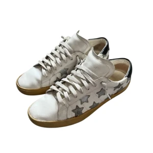 Saint Laurent sneakers - Coola vita sneakers från Saint Laurent med silvriga stjärnor på sidorna och svarta detaljer vid hälen. Skorna har beige sula och är gjorda i skinn med klassisk snörning. Perfekta för dig som vill sticka ut med en unik och trendig look.
