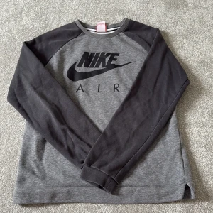 Nike Air grå sweatshirt XL kids - Snygg grå Nike Air sweatshirt med svarta ärmar och stort svart logotryck på bröstet. Tröjan har rund hals och långa ärmar, perfekt för chill eller sport. Mjuk och skön bomullsmix som passar dig som gillar streetwear.