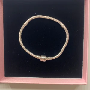 Pandora silverarmband med lås - Snyggt silverfärgat armband från Pandora med klassiskt vridet mönster och ikoniskt lås med Pandora-logga. Perfekt för att samla charms och skapa en personlig stil. Levereras i originalask och påse. Aldrig andvänd, säljer pga jag redan hade ett.Orginal pris 800kr
