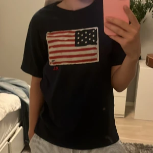 polo ralph lauren me usa flagga - mörkblå t-shirt från Ralph Lauren med stor amerikansk flagga tryckt på bröstet och diskret RL-brodyr i rött. Klassisk passform, rund hals och korta ärmar. Skön bomullskvalitet som passar perfekt till jeans eller shorts. Storleken är 14-16 år och är som S. Pris kan diskuteras vid snabbt köp. 